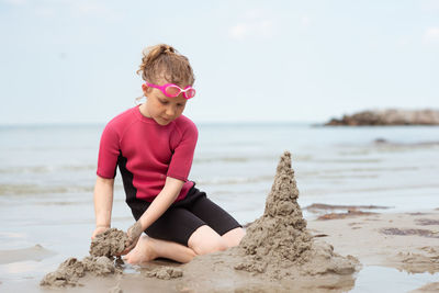 Full length of girl sitting on shore at beach against sky