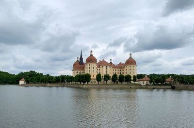 View of building by river against cloudy sky