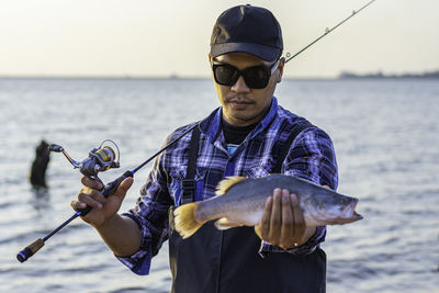 Portrait of young man holding fish in sea