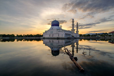 Mosque by lake against sky during sunset