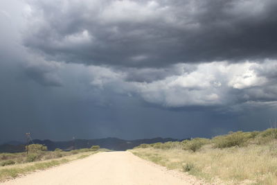 Road amidst landscape against storm clouds