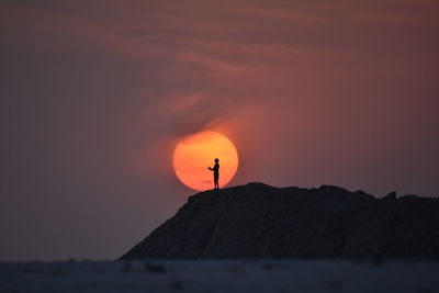 Silhouette man standing on rock against sky during sunset