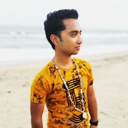 Young man looking away while standing on beach