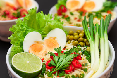 Noodle dish with green onions, eggs, green pea, red hot pepper, greens and lime