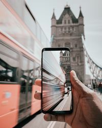 Cropped image of hand holding mobile phone in city