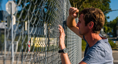 Profile of unhappy caucasian man leaning again outdoor fence.