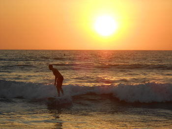 Man surfing in sea against sky during sunset