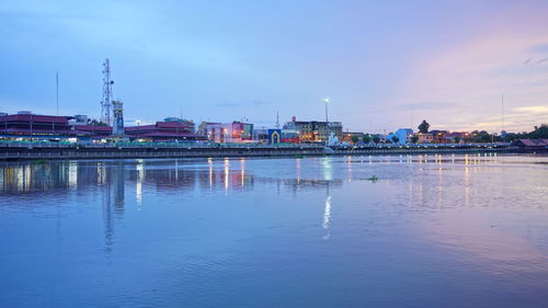 River by illuminated buildings against sky at dusk