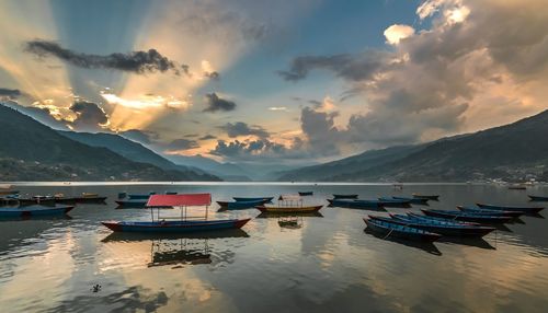 Boats moored in sea against sky during sunset