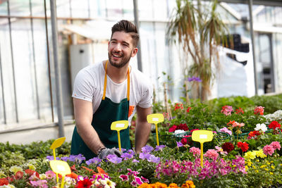 Young man smiling while standing by flower plants in green house