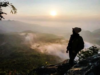 Man standing on rock against sky during sunrise