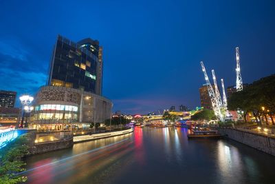 Illuminated buildings by river against sky at night