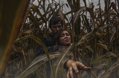 Portrait of young man holding woman neck amidst corns at farm during halloween