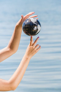 Close-up of woman hand holding ball in sea against sky