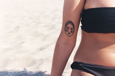 Midsection of woman with tattoo on hand at beach