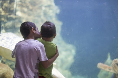 Rear view of brother kissing sibling while standing in aquarium
