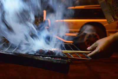 Cropped hand preparing meat on barbeque grill at night
