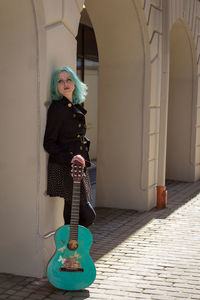Hipster young woman with turquoise guitar in city