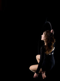 Side view of young woman standing against black background