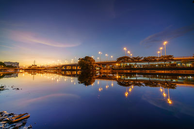 Illuminated city by river against sky at night