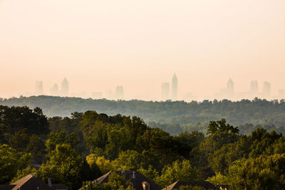 Trees and cityscape against sky during sunset