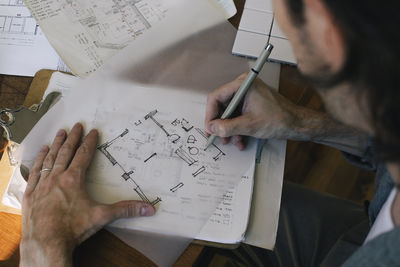 High angle view of male architect sketching blueprint on paper at desk in home office