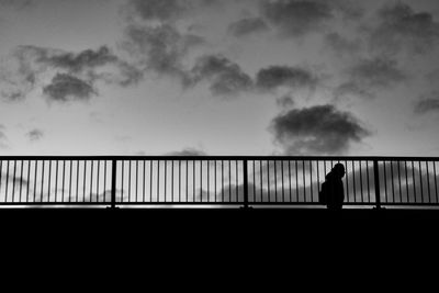 A silhouette standing on the bridge against the sky 