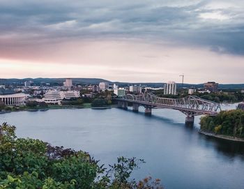 Bridge over river by buildings in city against sky