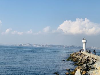 Lighthouse by sea and buildings against sky