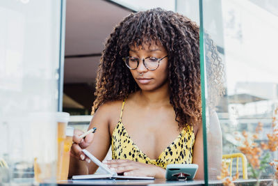 Black self employed woman sitting at table in cafe and working remotely while writing in notepad