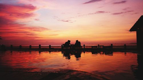 Silhouette people on sea against orange sky