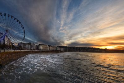 Amusement park by sea against sky during sunset
