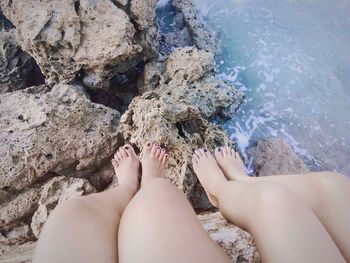 Low section of women sitting on rock on shore in sea