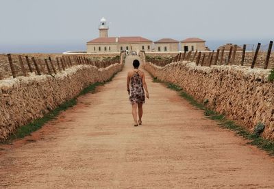 Rear view of woman walking amidst buildings against sky