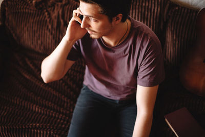 Young man talking on mobile phone sitting on sofa at home