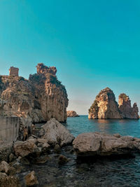 Rocks in sea against clear blue sky