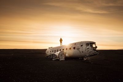 Man standing on abandoned airplane against sky during sunset