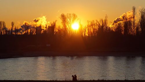 Silhouette trees by lake against sky during sunset