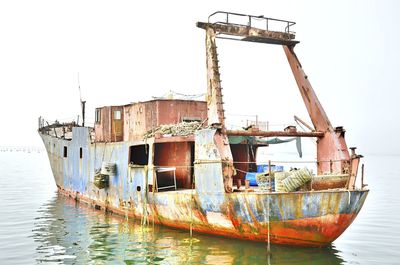 Old boat moored in sea against clear sky