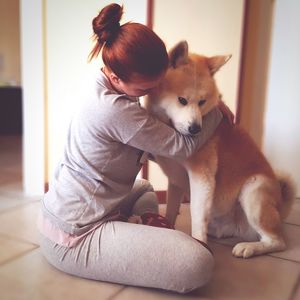 Woman embracing akita while sitting on floor at home