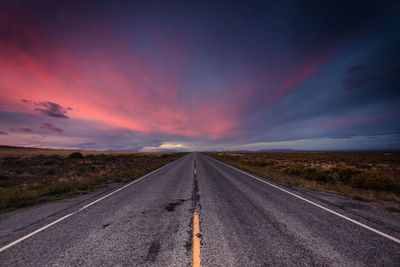 Empty road amidst landscape against sky during sunset