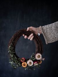 Cropped hand of woman holding flower decoration against black background