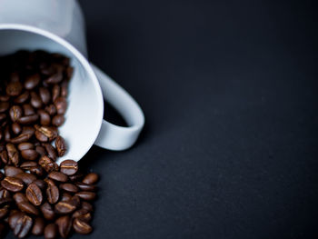 Close-up of roasted coffee beans spilling from cup on table