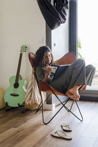 Girl using digital tablet while sitting on chair by guitar on home