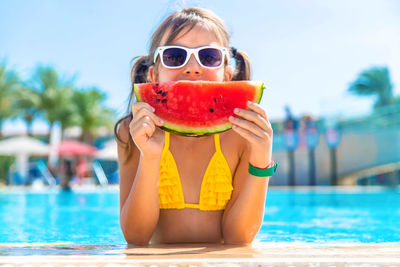 Portrait of smiling girl with watermelon by swimming pool