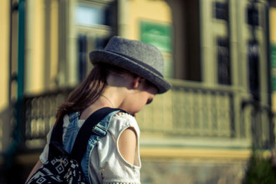 Girl in sun hat looking down against buildings