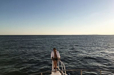 Full length of man standing on boat in sea against clear sky during sunset