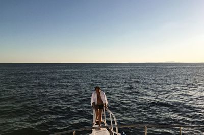 Rear view of man standing on sea against clear sky