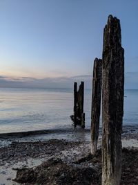 Wooden posts on beach against sky during sunset