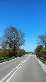 Road amidst trees against clear blue sky